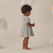 Young child in a striped dress standing against a neutral background