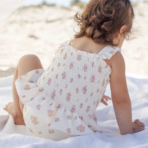 Child in a floral dress sitting on a sandy beach