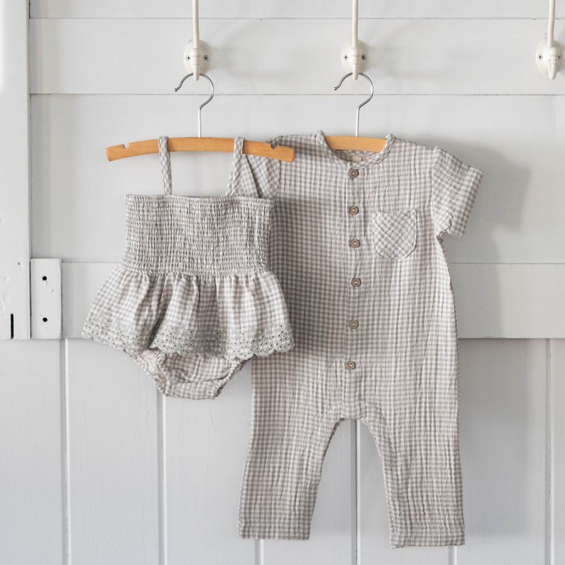 Baby romper and top set hanging on a rack against a white wall.