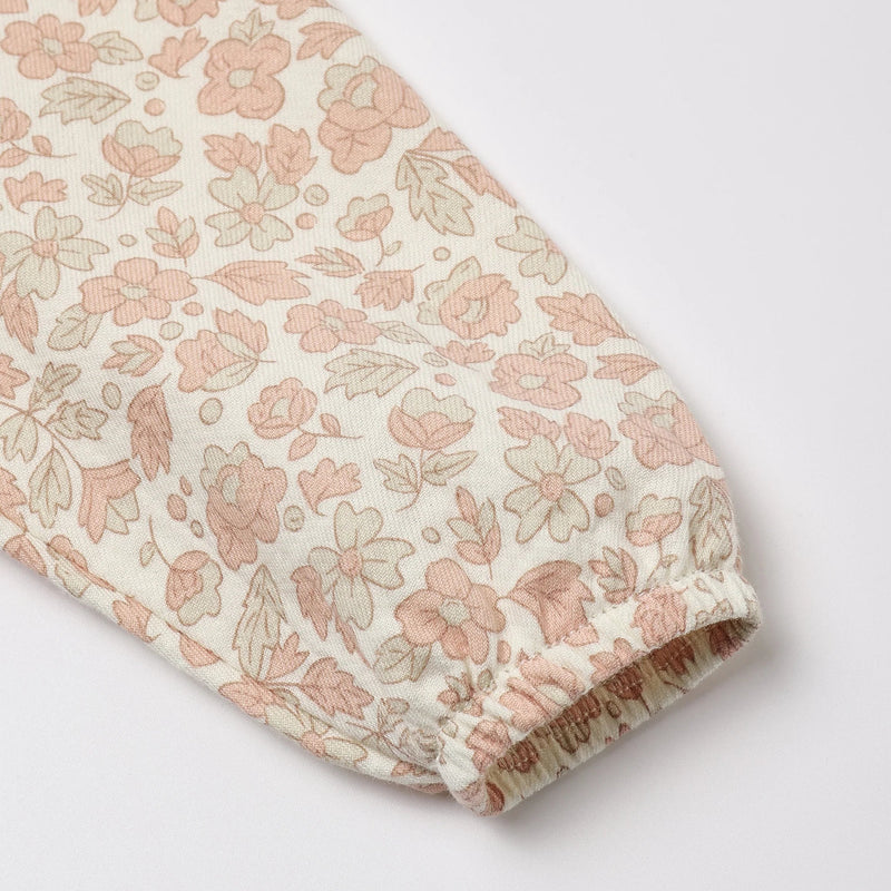 A close-up of a long sleeve featuring an all-over delicate floral and leaf print in soft pink and muted green on an off-white background, finished with a gathered elastic cuff.