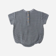 Textured baby romper with button details on a light gray background
