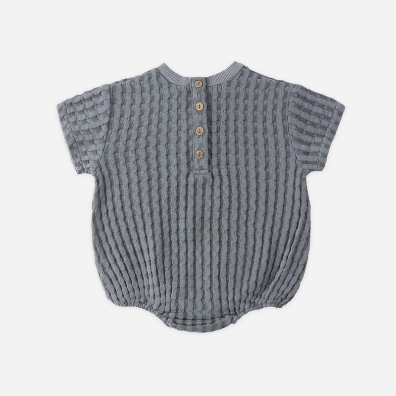 Textured baby romper with button details on a light gray background