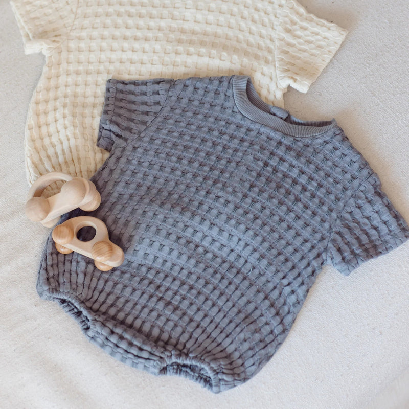 Baby outfit with beige top and blue shorts on a light surface