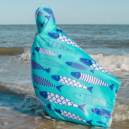 Person wearing a turquoise poncho with fish pattern on a beach