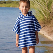 Child wearing a blue and white striped hooded towel by a body of water.