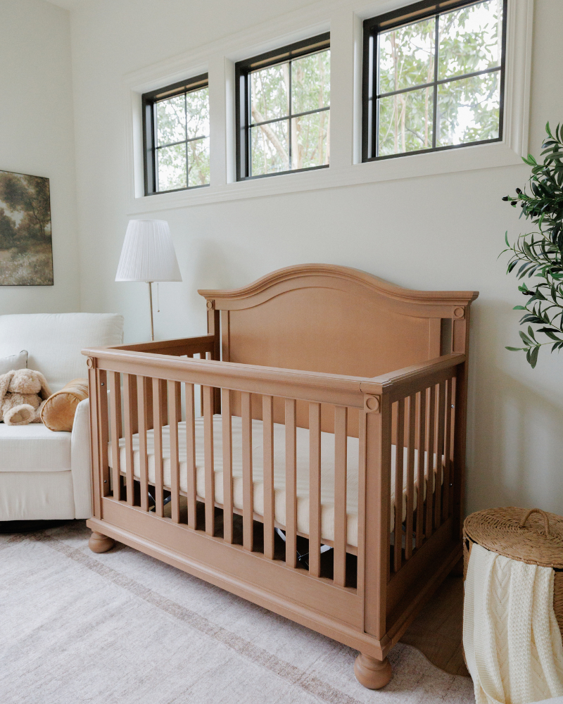 Wooden crib in a nursery with white walls and a couch.