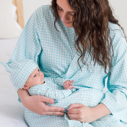 Woman in a light blue checkered robe holding a baby in a matching outfit on a white bed.