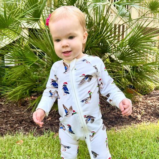 Toddler standing outdoors wearing Saltwater Swaddles Duck The Halls bamboo footie covered in festive ducks with Santa hats
