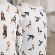 Two mannequins wearing white shirts with animal pattern, including dogs and ducks wearing santa hats, on a blurred background.