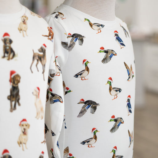 Two mannequins wearing white shirts with animal pattern, including dogs and ducks wearing santa hats, on a blurred background.