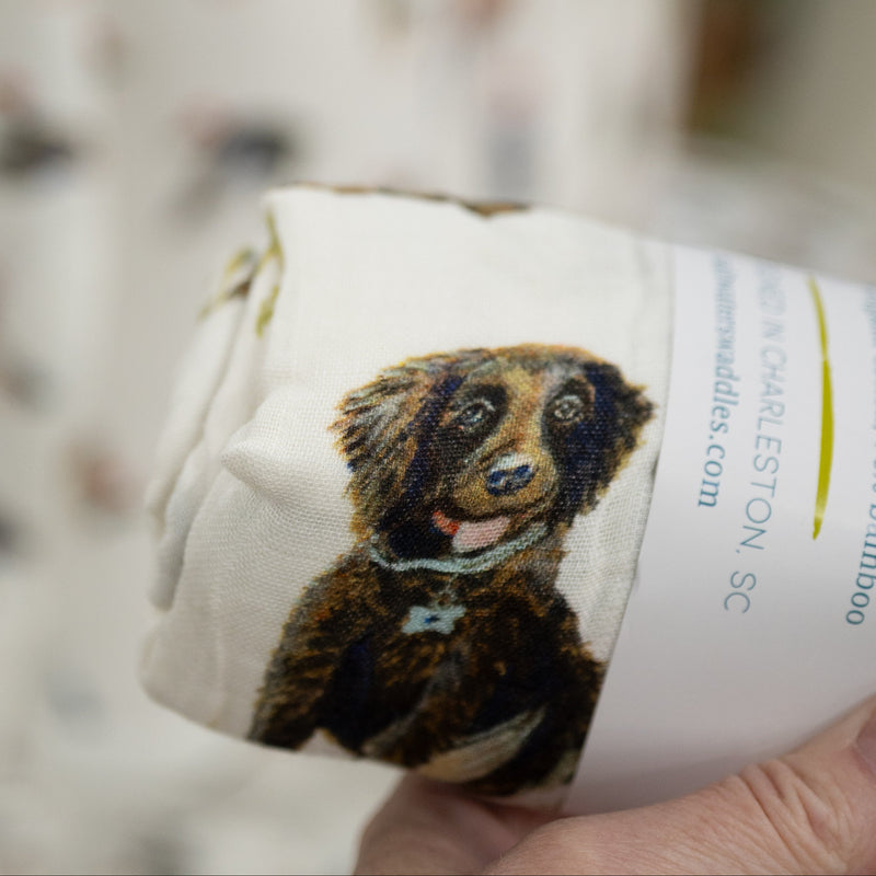 White muslin swaddle blanket with a boykin spaniel dog illustration on a label held by a person.
