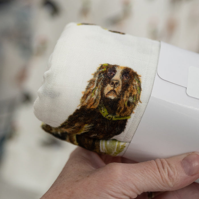 White muslin swaddle blanket with a boykin spaniel dog illustration held by a person, blurred background