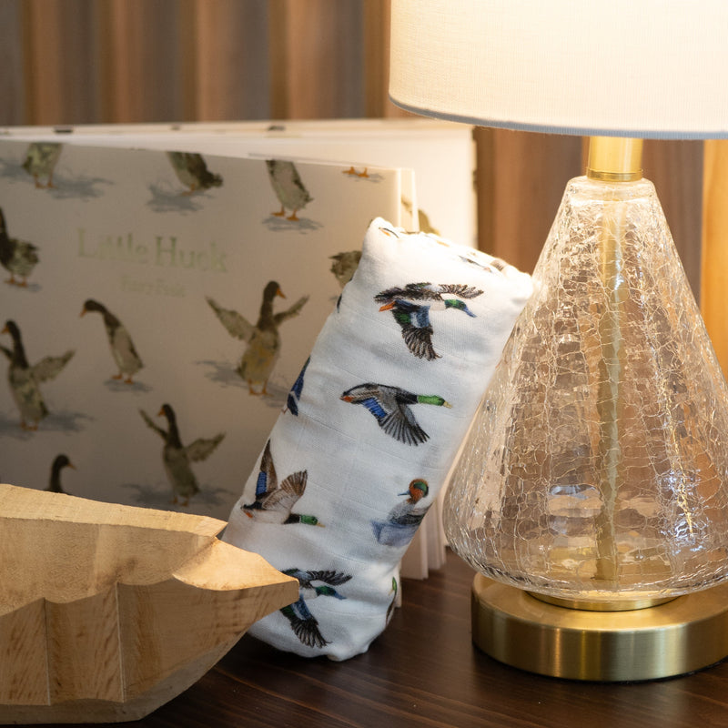 Decorative lamp on a wooden surface with a duck patterned rolled swaddle blanket and wooden panel background