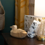 Wooden duck figurine, lamp, and ducjk patterned swaddle blanket on a table with curtains in the background.