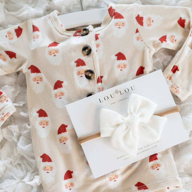 Baby outfit with Santa Claus pattern and a white bow on a textured surface