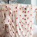 Children's pajamas with red santa patterns on a hanger against a neutral background