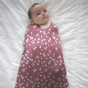 A newborn sleeps on a white surface wearing the Mini Floral Sleep Sack Swaddle fully zipped.