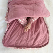 A baby lies inside the unzipped swaddle, feet visible, showing the roomy interior and quilted lining.