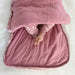 A baby lies inside the unzipped swaddle, feet visible, showing the roomy interior and quilted lining.