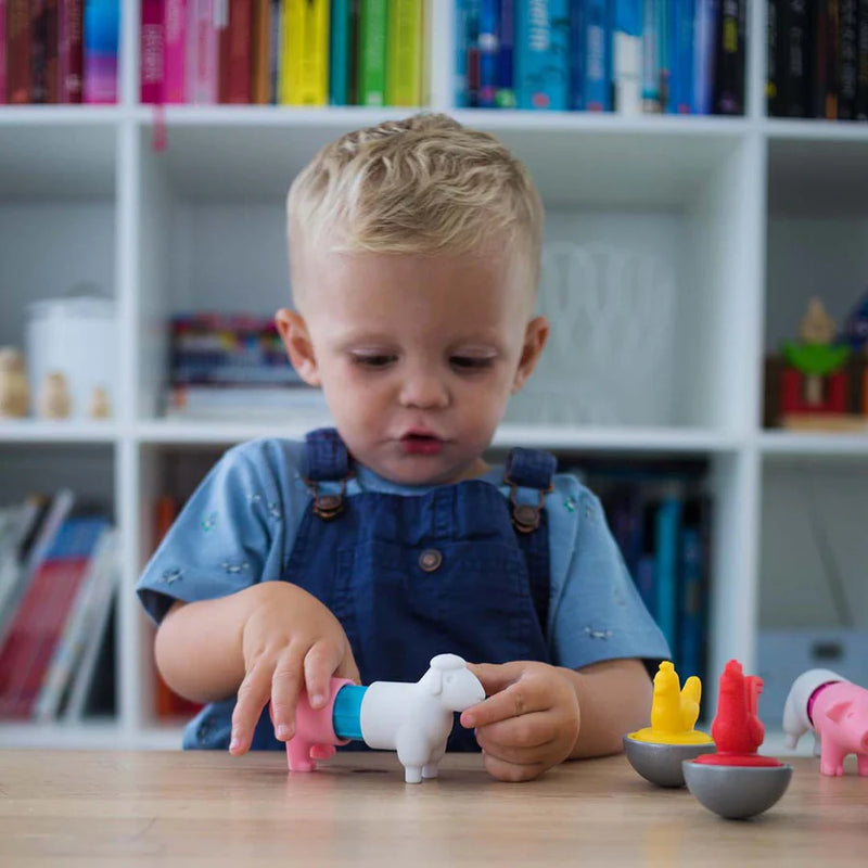 Child playing with colorful animal toys on a table in front of a bookshelf.
