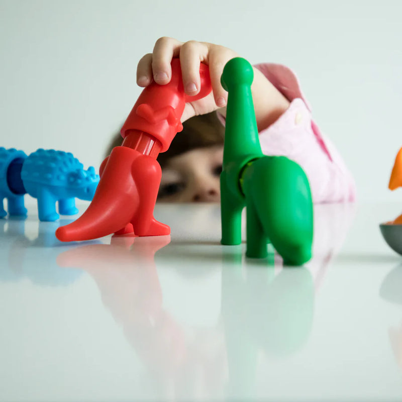 Colorful dinosaur toys on a reflective surface with a child's hand interacting with them.