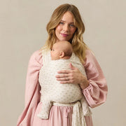 Woman holding a baby wrapped in a white wrap against a beige background