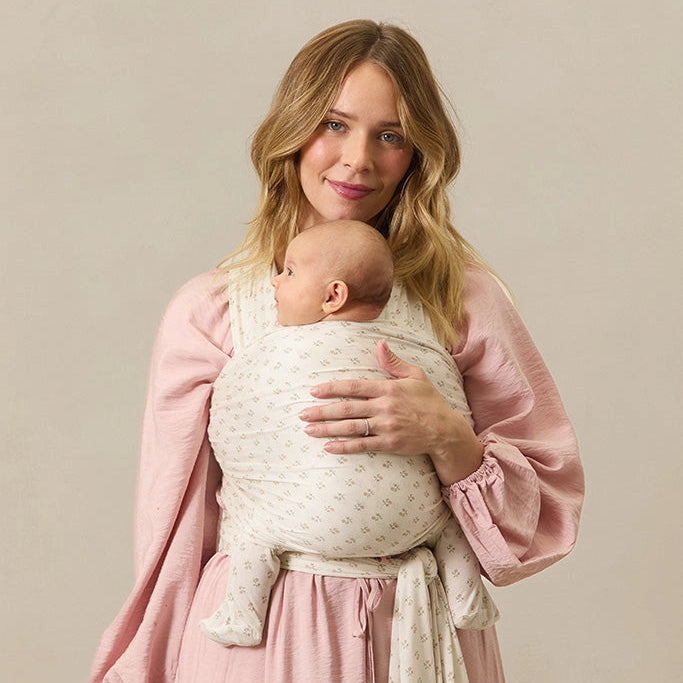 Woman holding a baby wrapped in a white wrap against a beige background