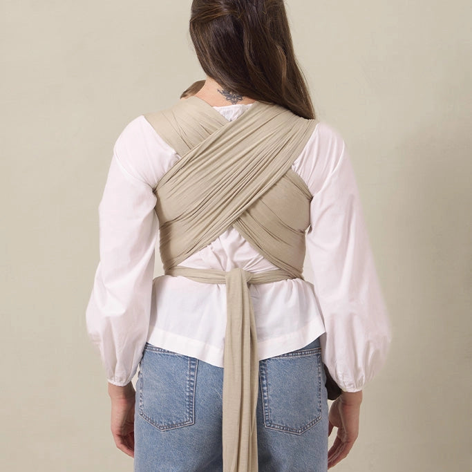 Person wearing a beige wrap over a white shirt and blue jeans on a beige background