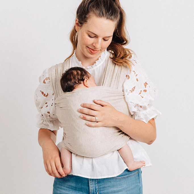 Woman holding a baby in a sling against a white background