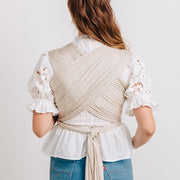Woman wearing a beige wrap over a white blouse and blue jeans on a plain background
