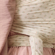 Baby in a floral outfit being held by a person wearing a pink dress.