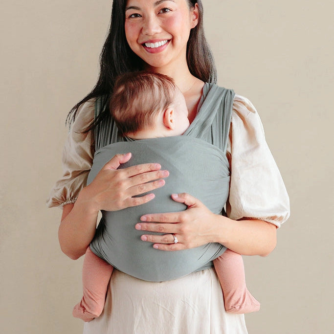 Woman holding a baby in a  carrier against a beige background