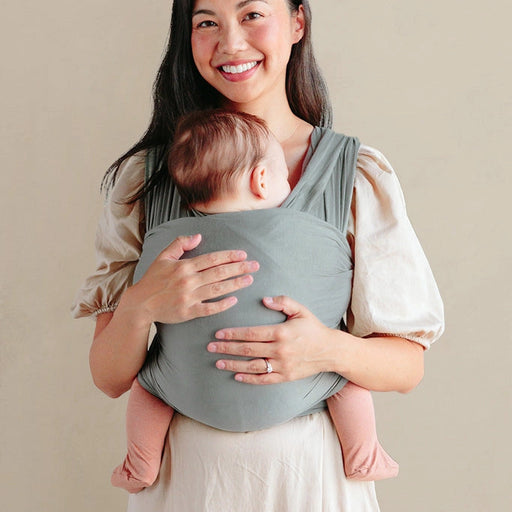 Woman holding a baby in a  carrier against a beige background