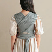 Woman wearing a light-colored dress with a gray wrap over her shoulders against a beige background