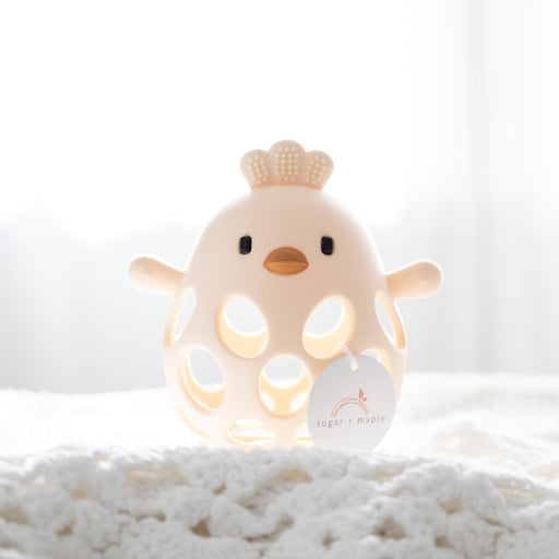 Yellow baby teether shaped like a chick on a soft white surface