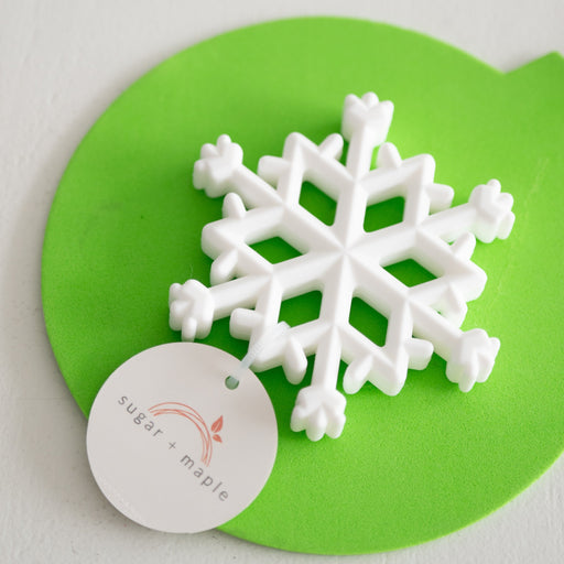 White snowflake-shaped teether on a green mat with 'sugar & Maple' label.