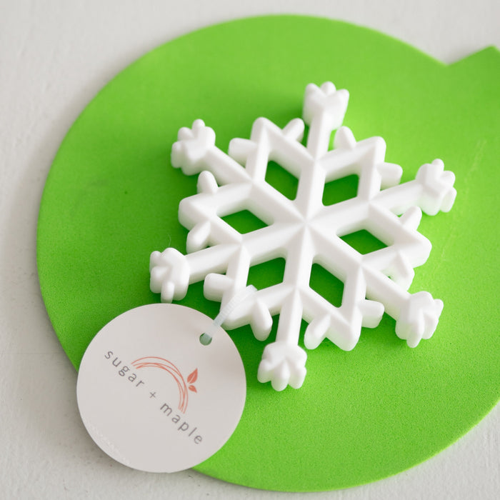 White snowflake-shaped teether on a green mat with 'sugar & Maple' label.
