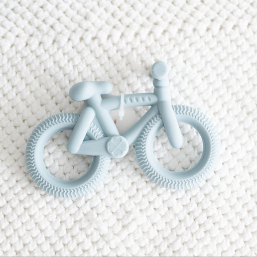 Blue bicycle-shaped teether on a textured white surface
