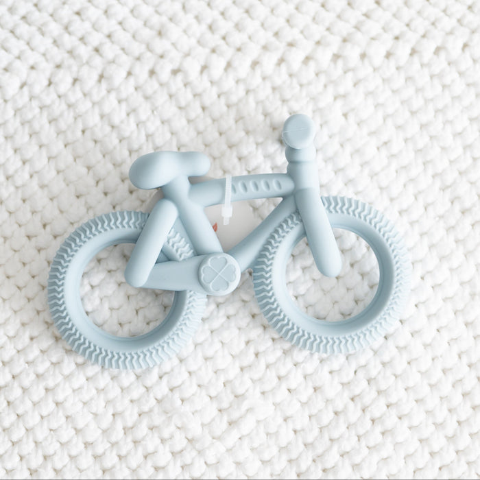 Blue bicycle-shaped teether on a textured white surface