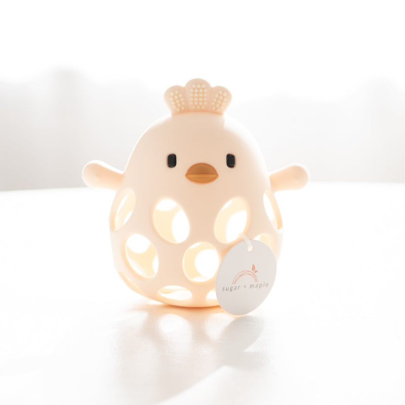 yellow silicone chick teether on a white surface with a blurred background