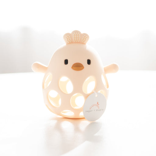 yellow silicone chick teether on a white surface with a blurred background