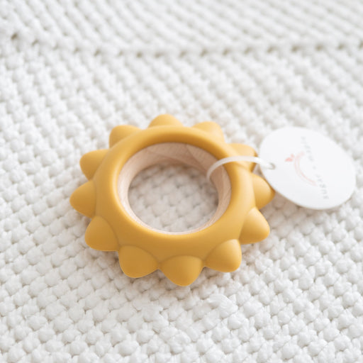 Yellow sun-shaped teething ring on a white textured surface