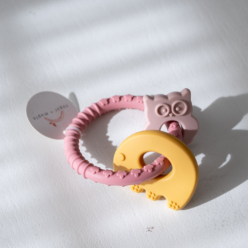 Pink and yellow teething ring with elephant and owl design on a light background