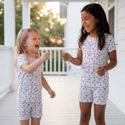 Two children in matching pajamas holding sparklers on a porch.