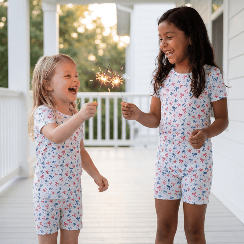 Two children in matching pajamas holding sparklers on a porch.