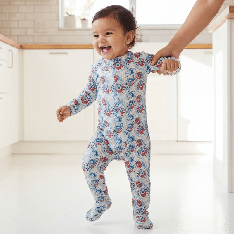 Baby in a floral onesie being held by an adult in a bright room.
