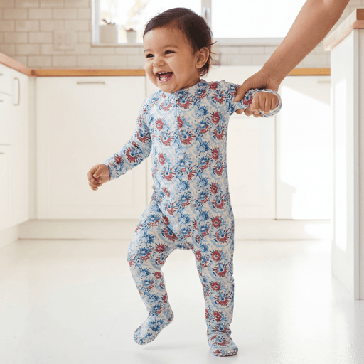 Baby in a floral onesie being held by an adult in a bright room.
