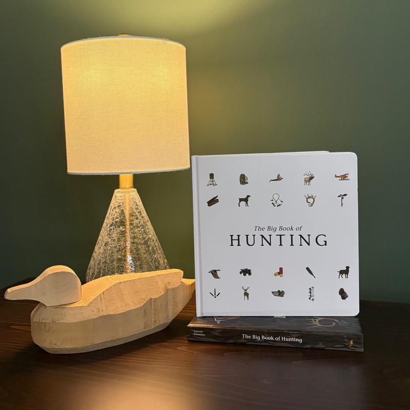 Wooden duck decoy and book titled 'The Big Book of Hunting' on a dark surface with a green background.
