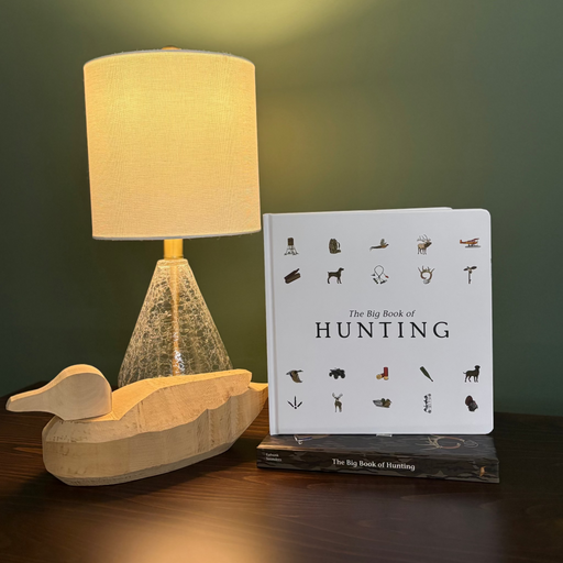 Wooden duck decoy and book titled 'The Big Book of Hunting' on a dark surface with a green background.
