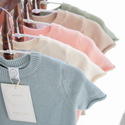 Row of baby sweaters on hangers with visible lou lou and company brand tag.